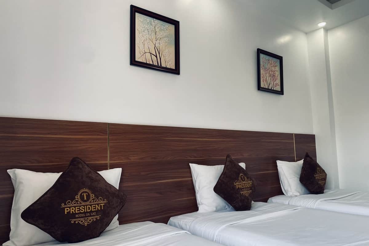 A hotel room with a wooden headboard, white bedding, and decorative pillows with "PRESIDENT HOTEL" text.