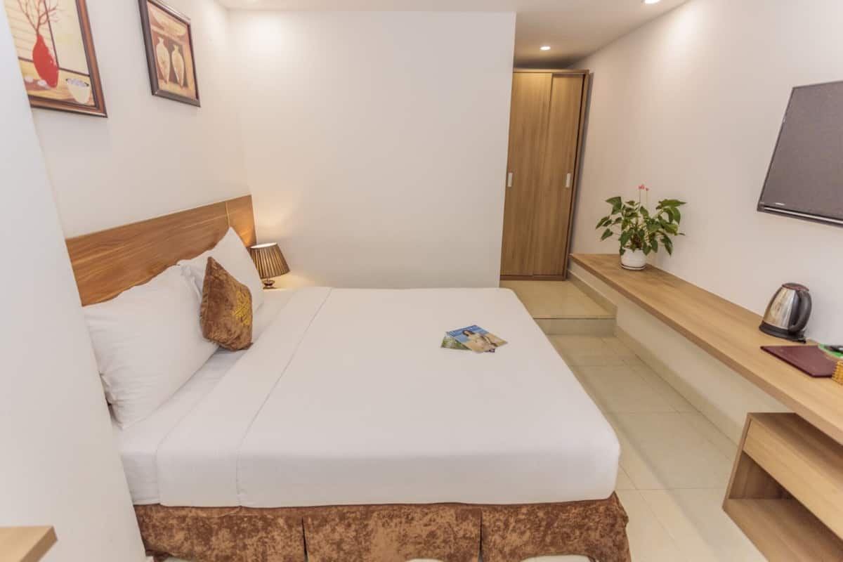 A neatly arranged hotel room with a bed, bedside lamp, a small table with a plant, and a TV mounted on the wall.