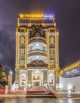 Un hotel con un llamativo letrero que dice 'President', una entrada imponente con escalones y un balcón con barandillas.