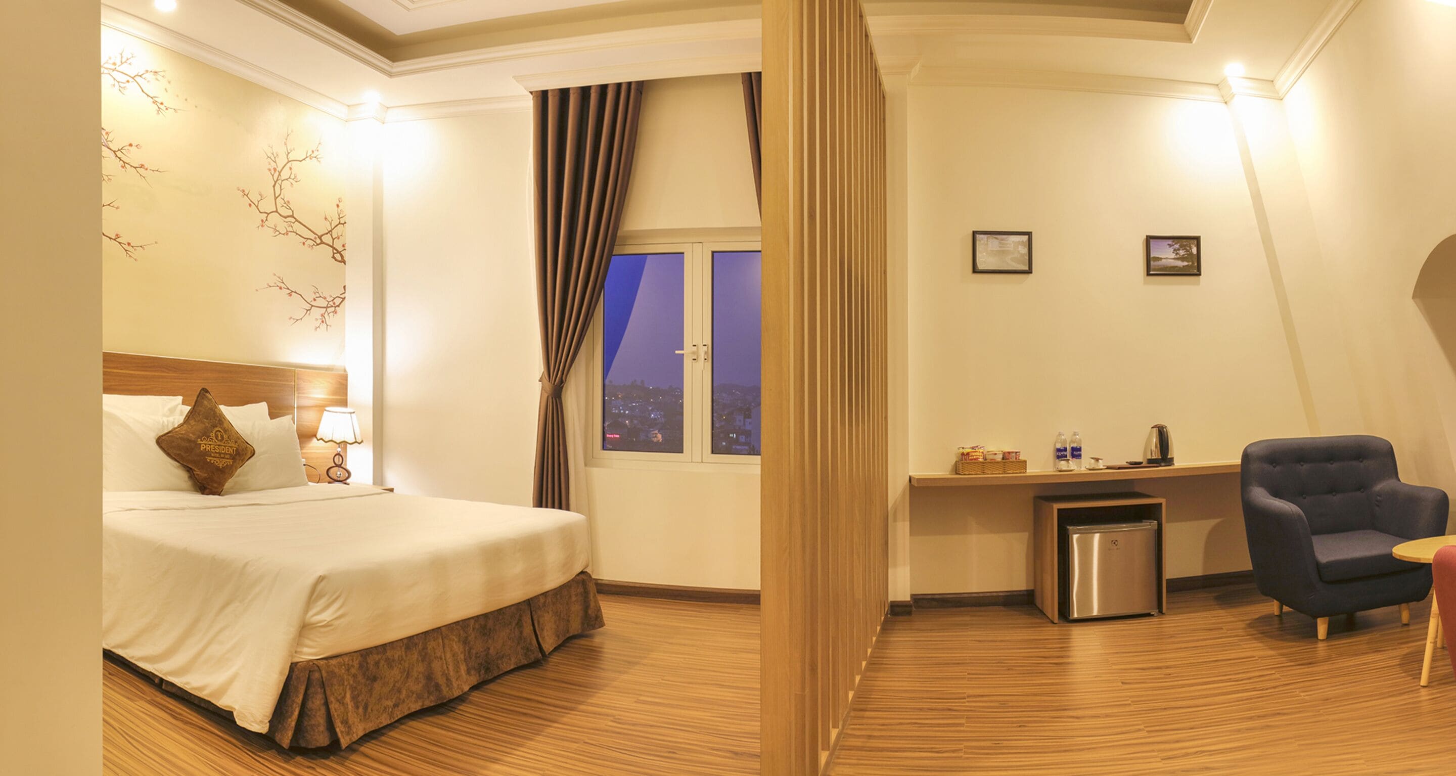 Une chambre d’hôtel équipée d’un lit, d’un bureau, d’une chaise, d’un petit réfrigérateur et d’une fenêtre avec des rideaux.