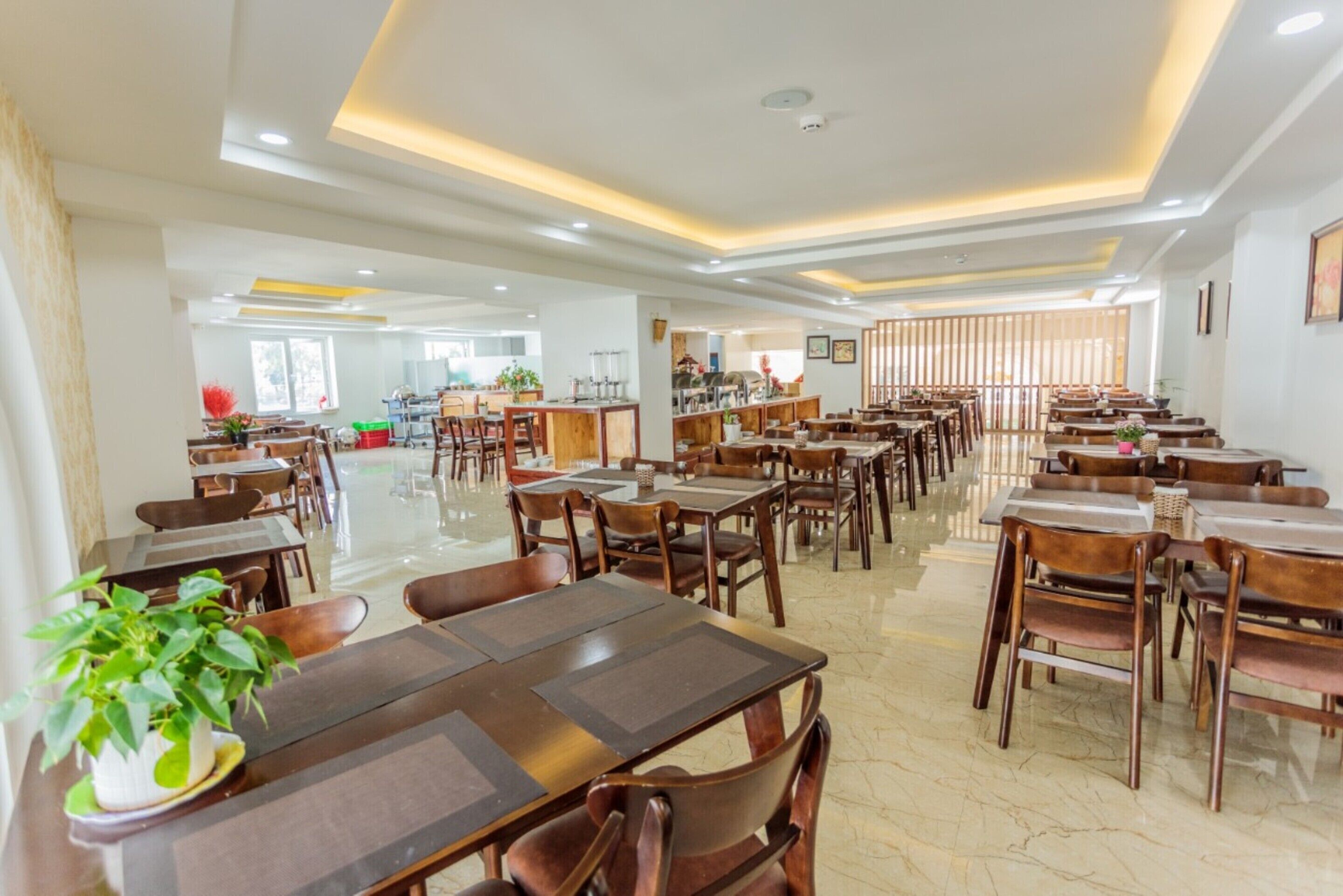 Un vaste espace de salle à manger avec de nombreuses tables et chaises, un espace cuisine central et un design de plafond moderne.