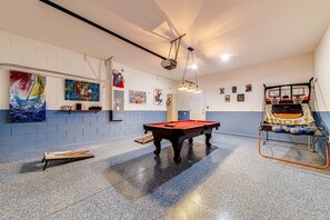 Ein Billardtisch in einem Raum mit einem Basketballkorb, Kunstwerken an den Wänden und einem Deckenventilator.