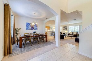 Un intérieur spacieux comprenant un coin repas, une cuisine et un salon, avec un plafond haut et de grandes fenêtres.