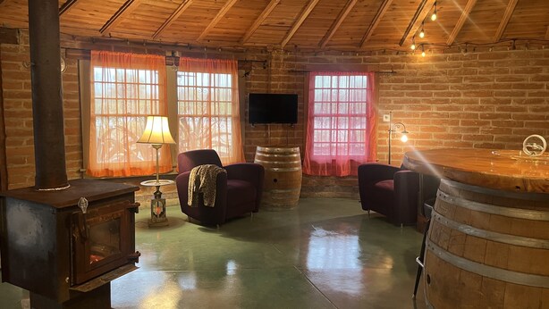 A rustic room with a wooden ceiling, a fireplace, two armchairs, a television, and a bar counter.