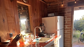 A rustic kitchen with wooden walls, a tiled countertop, a sink, and a refrigerator.