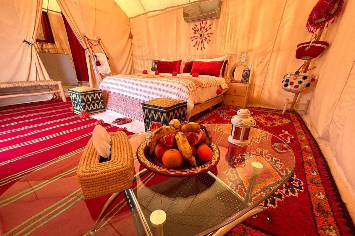 A tented room with a bed, a table with a fruit bowl, and a woven basket.