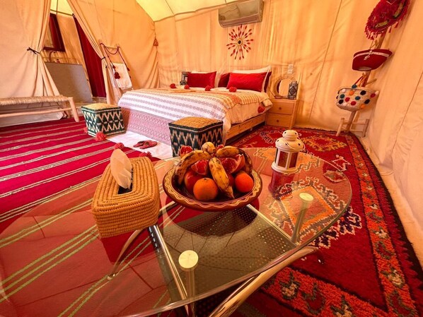 A tented room with a bed, a table with a fruit bowl, and a woven basket.