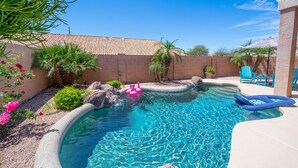 A swimming pool with clear blue water, surrounded by a brick wall, palm trees, and a small garden with pink flowers. - Rare 3 FULL bathroom home in golf community W/ private pool. Experienced Host. (Mesa)