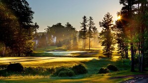 Un campo de golf con un sendero de piedra, árboles y un edificio al fondo.