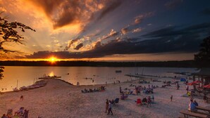 Una playa con un atardecer, barcos y gente relajándose.