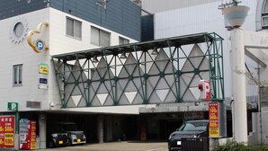 Ingang van een parkeergarage met een groen metalen luifel, een zwarte auto die er geparkeerd staat, en een bord met parkeertarieven.
