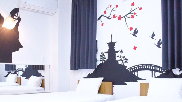 Een hotelkamer met twee bedden, een grote spiegel en een muurschildering van een Japanse tempel en kersenbloesems.