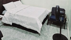 A bedroom with a bed, a standing fan, and a ceiling light. - Motalvin Court  (Lagos)
