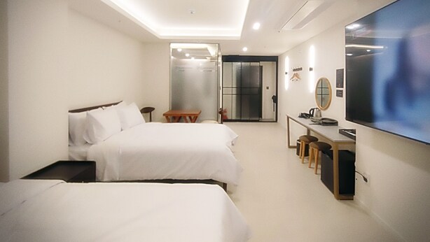 A hotel room with two beds, a desk with a chair, a TV, and a sliding door leading to a bathroom.