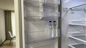 Een moderne hotelkamer met een ingebouwde koelkast, een eethoek met een stoel en uitzicht op de gang.