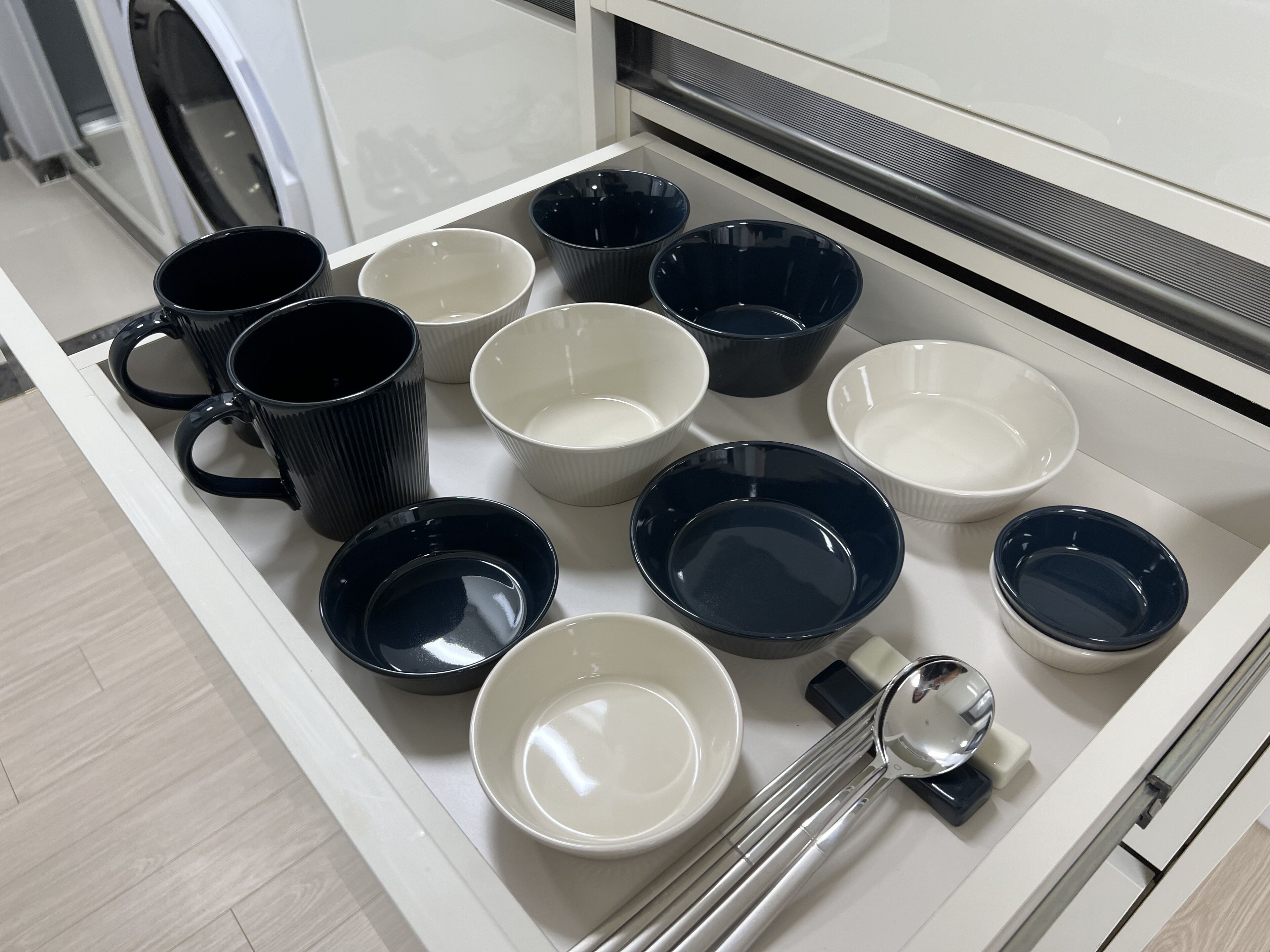 Un tiroir de cuisine contenant divers bols et tasses, un grille-pain et une bouilloire.