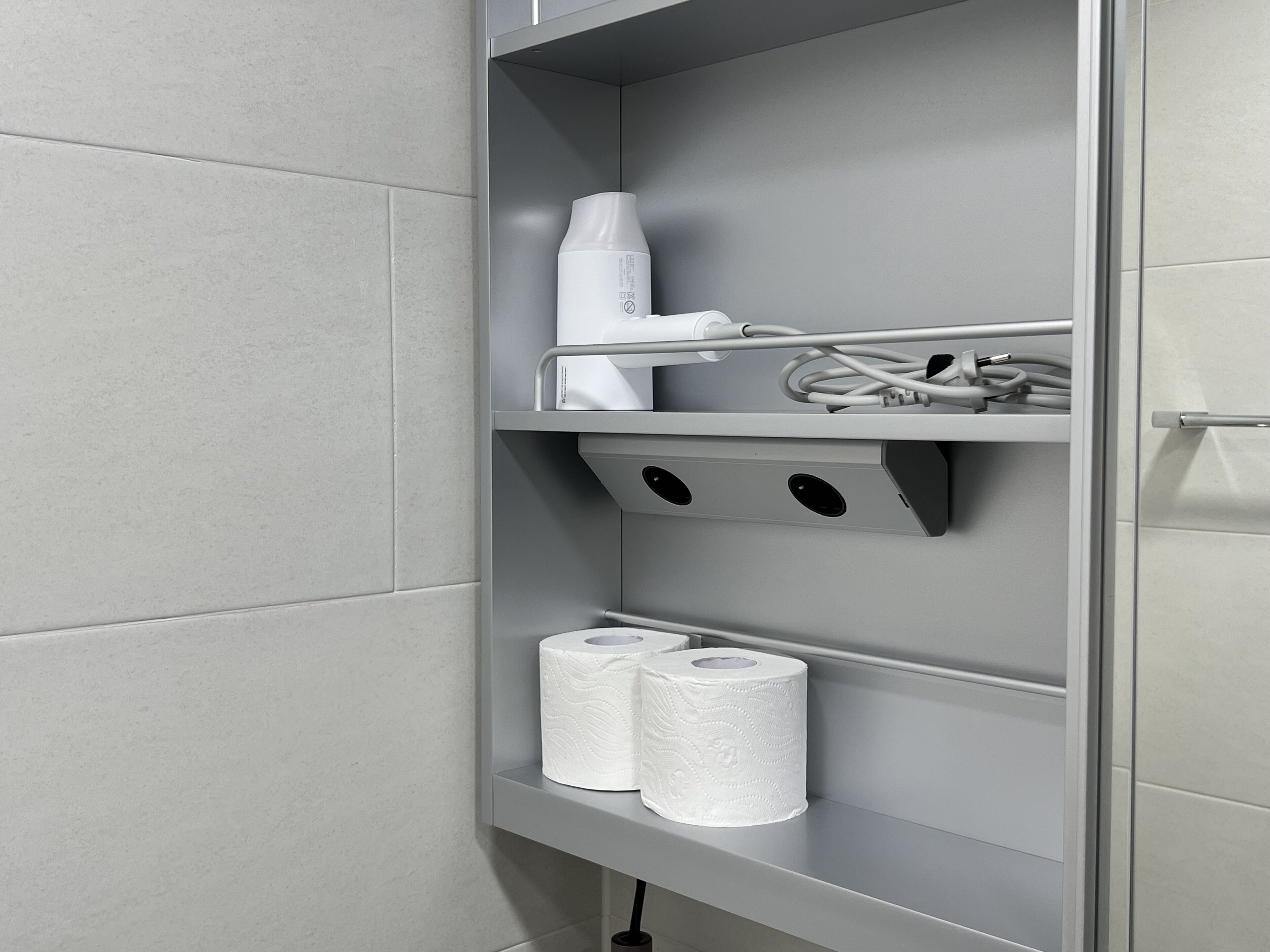 Een badkamer met een toiletrolhouder, een haardroger en een handdoekrek.