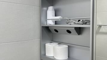 Een badkamer met een toiletrolhouder, een haardroger en een handdoekrek.