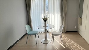 A modern hotel room with a round dining table, two chairs, a vase with flowers, and a large window with sheer curtains. - HoyaStay (Yeosu)