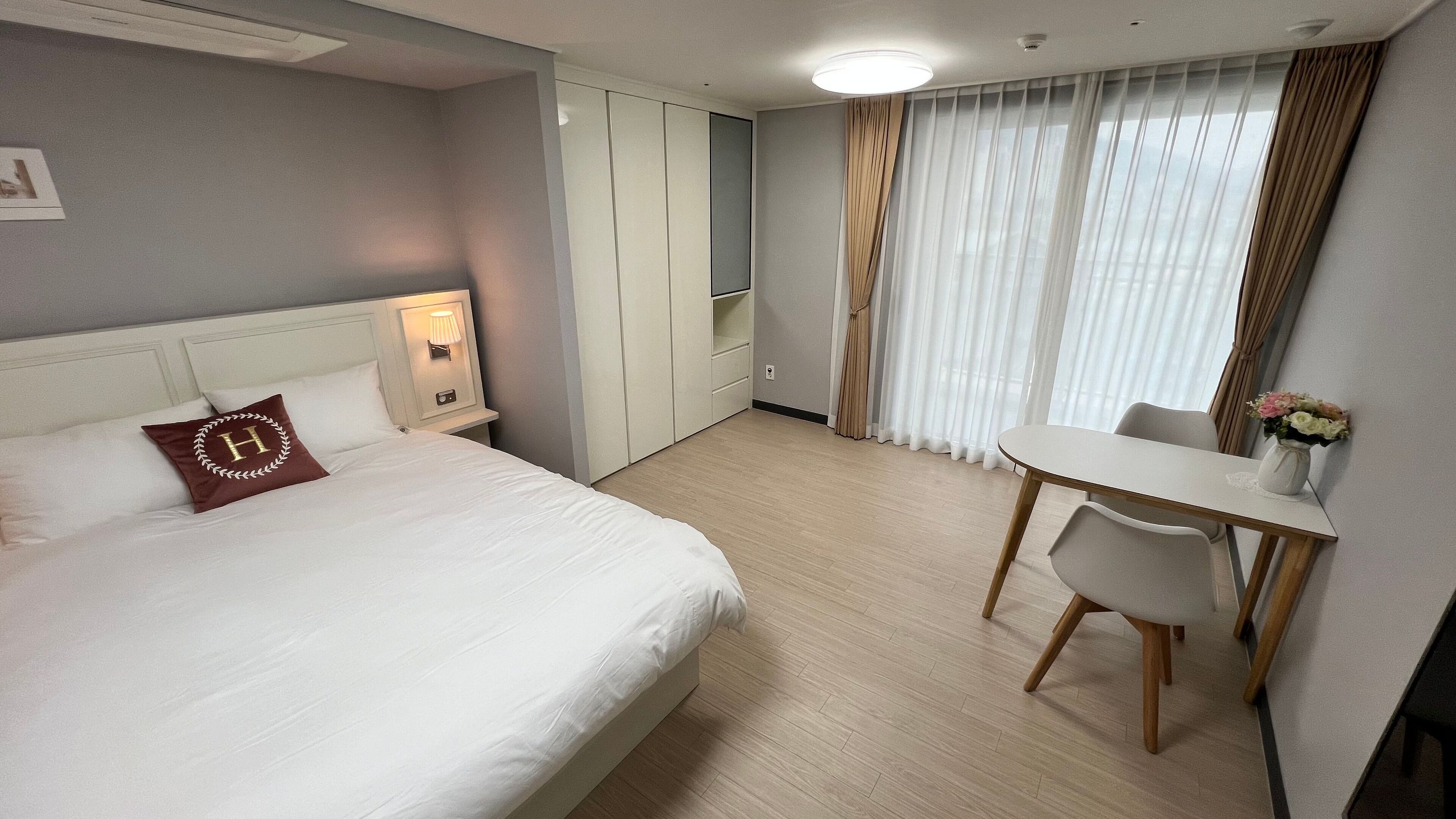 Habitació d'hotel amb un llit, una taula de nit, una làmpada, cortines i una taula petita amb cadires.