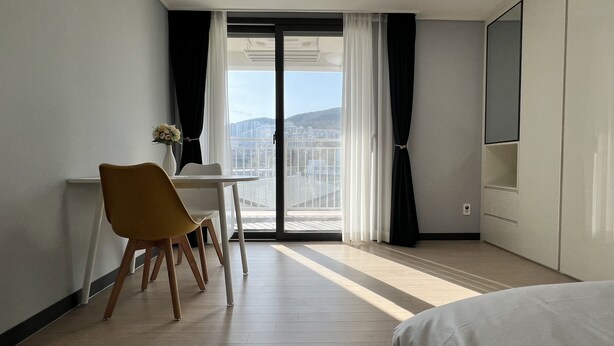 A hotel room with a balcony, a dining table with chairs, a bed, and a TV. - HoyaStay (Yeosu)