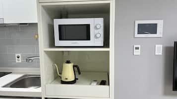 Una cocina con microondas en un estante, tetera y cafetera.