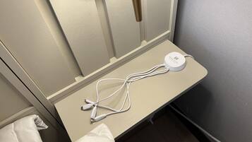 A bedside table with a white charging station and cables, a pillow, and a wall-mounted lamp.