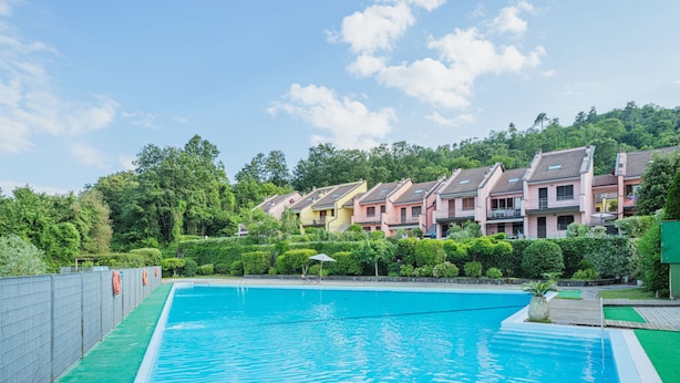 A swimming pool with a green deck, surrounded by a fence with life rings. In the background, there are multi-story buildings with balconies. - Villaggio 5 Terre by Interhome (Pignone)