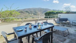 An outdoor dining area with a table set for two, overlooking a scenic view of hills and a body of water. - Villaggio 5 Terre by Interhome (Pignone)