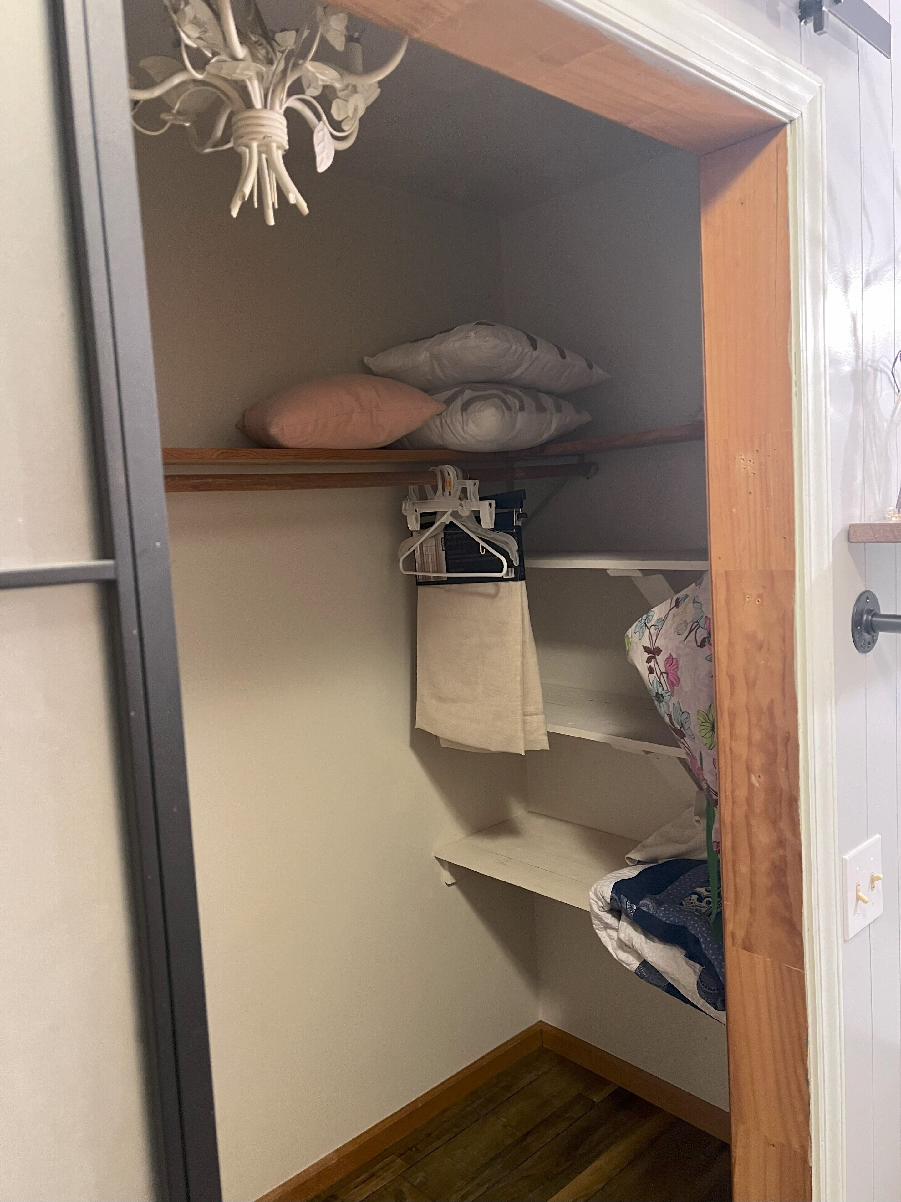 A compact room with a bunk bed, a hanging light fixture, and a wooden shelf.
