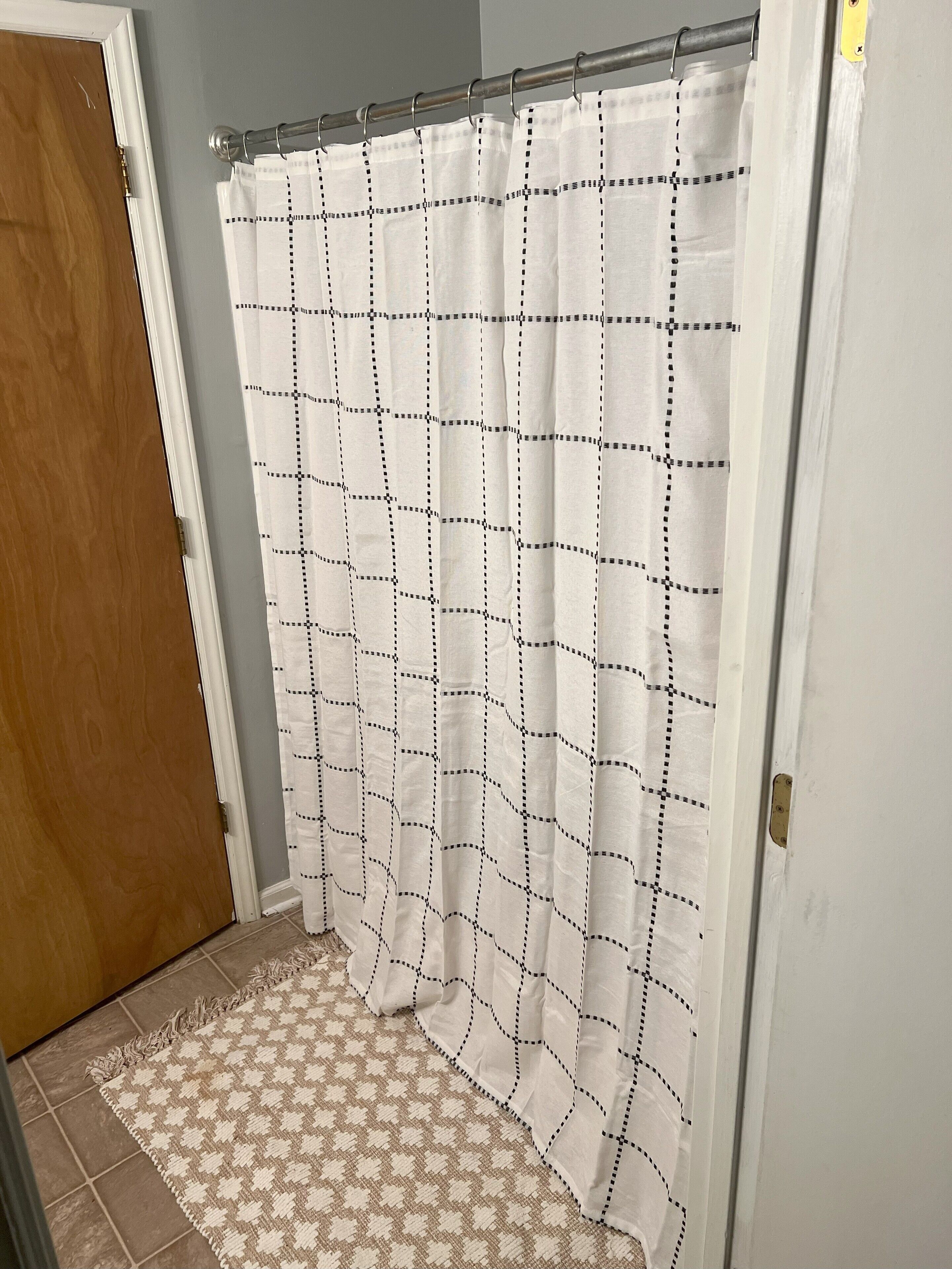 A bathroom with a shower curtain featuring a grid pattern, a wooden door, and a patterned rug on the floor.