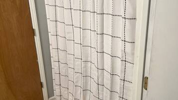 Une salle de bain avec un rideau de douche orné d’un motif à carreaux, une porte en bois et un tapis à motifs sur le sol.