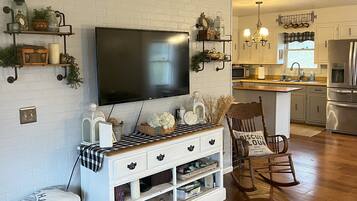 A modern living room with a flat-screen TV, wooden entertainment unit, and a cozy seating area with a rocking chair.