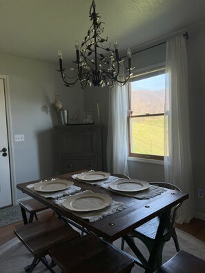 A dining room with a wooden table set for four, a chandelier, and a window with a view of a field. - Mountain House near the Appalachian Trail, Watauga Lake, Bristol, & Johnson City (Hampton)