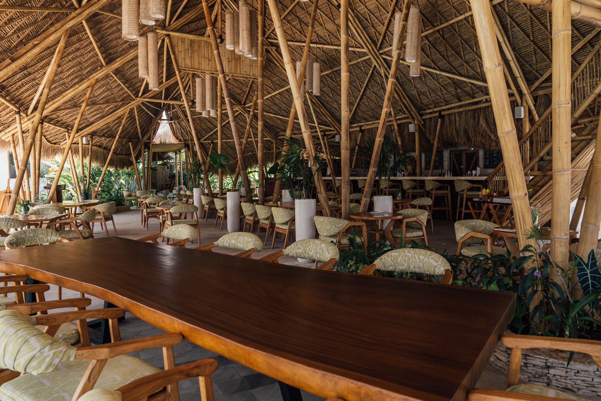 Un restaurante de estilo bambú con techos altos, mesas de madera y sillas acolchadas.