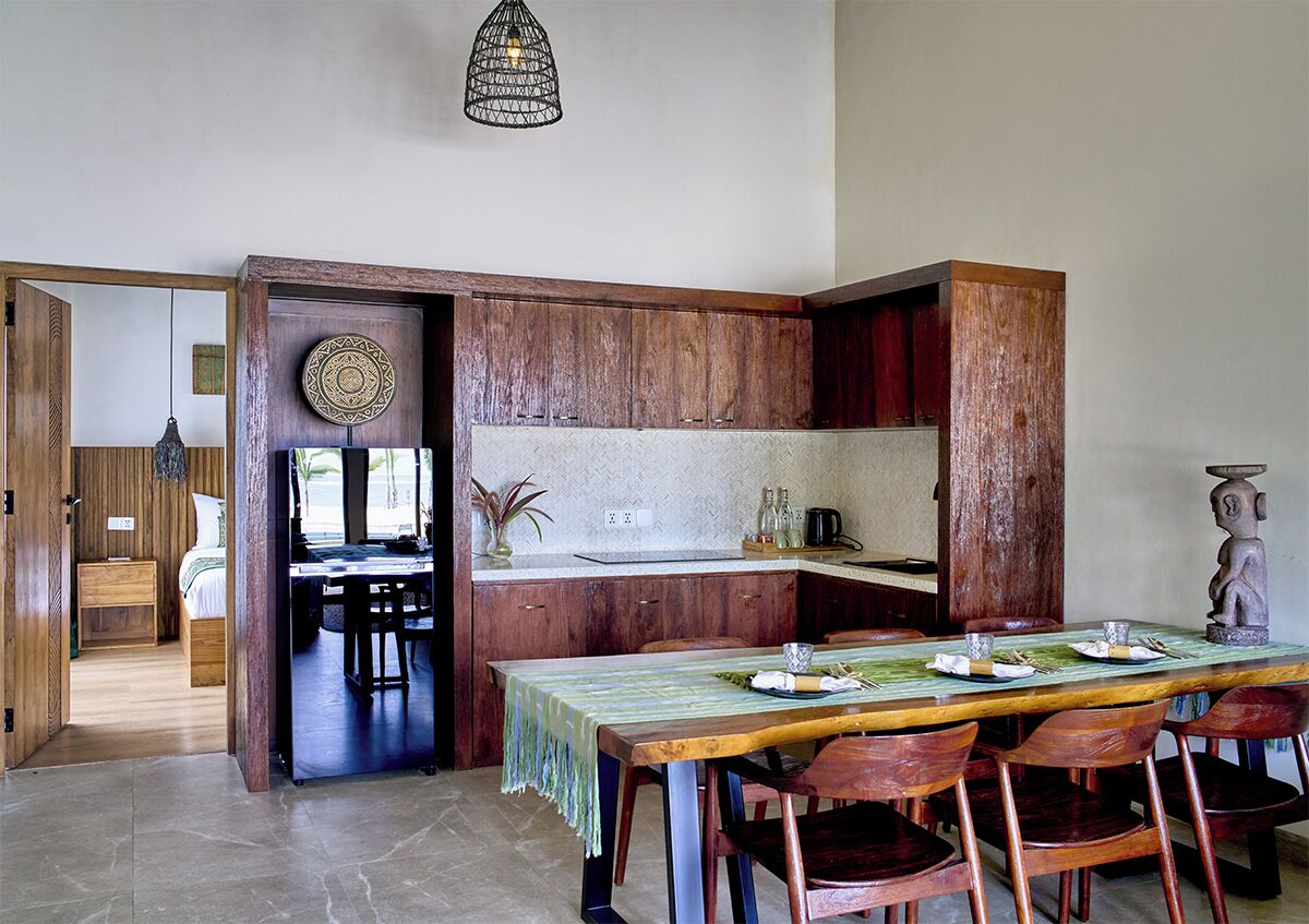 A compact kitchen with wooden cabinets, a dining table set for four, and a hanging light fixture.