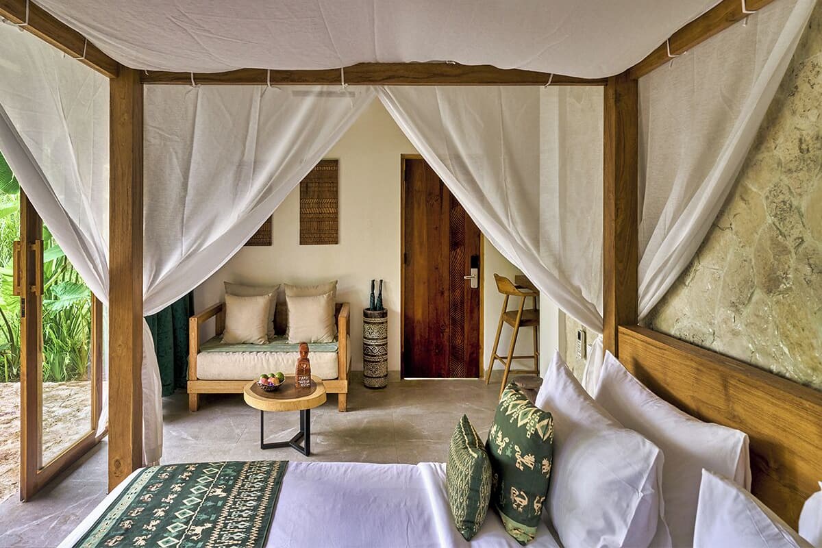 Una habitación con una cama, un sofá, una mesita y una silla. Hay una puerta y una ventana.
