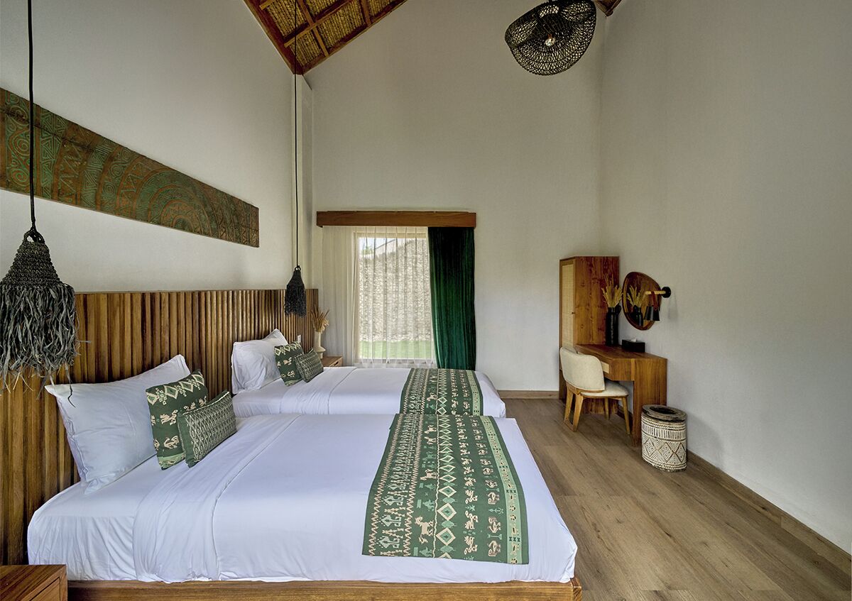 A bedroom with two beds, a desk, a chair, and a hanging light fixture.