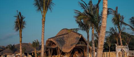 A beachside resort with thatched-roof structures, lounge chairs, and palm trees.