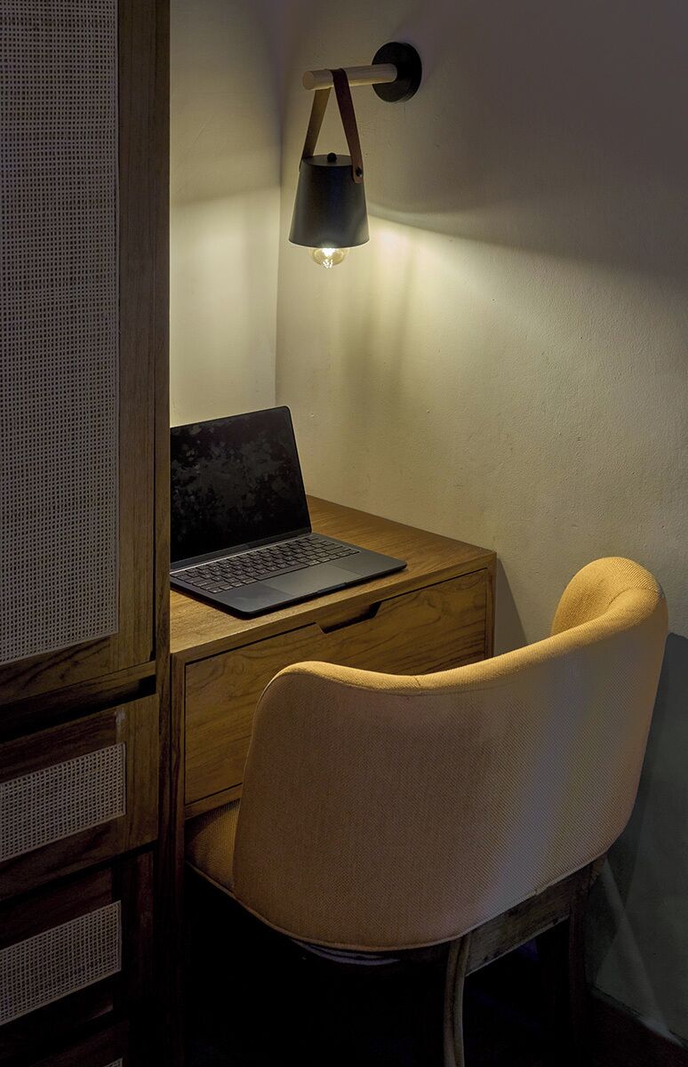 Escritorio de madera con una laptop, una lámpara y una silla en una habitación con pared texturizada.