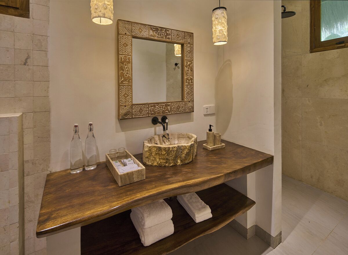 Un baño con tocador de madera, un espejo decorativo y un estante empotrado con toallas.