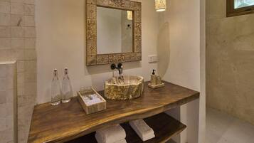 Un baño con tocador de madera, un espejo decorativo y un estante empotrado con toallas.