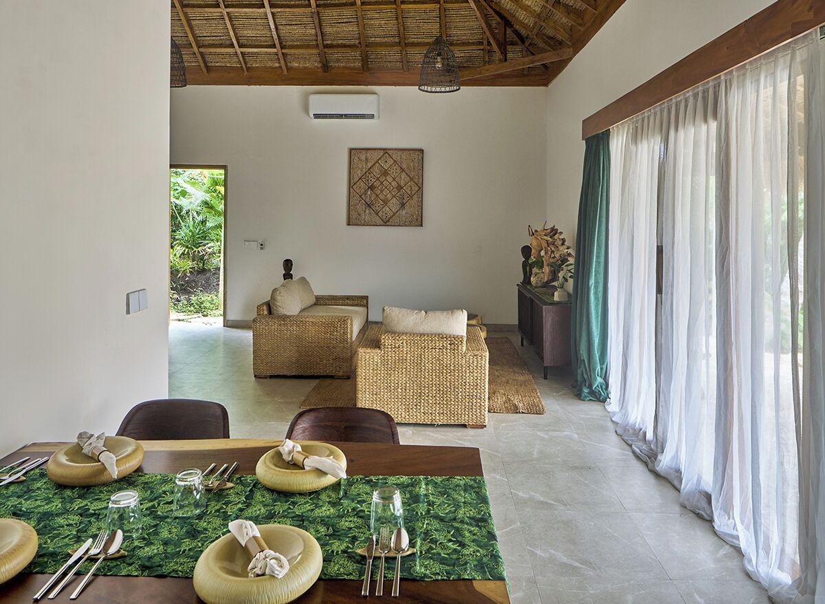 A dining area with a table set for four, a wicker sofa, and a view of greenery through the window.