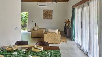 A dining area with a table set for four, a wicker sofa, and a view of greenery through the window.
