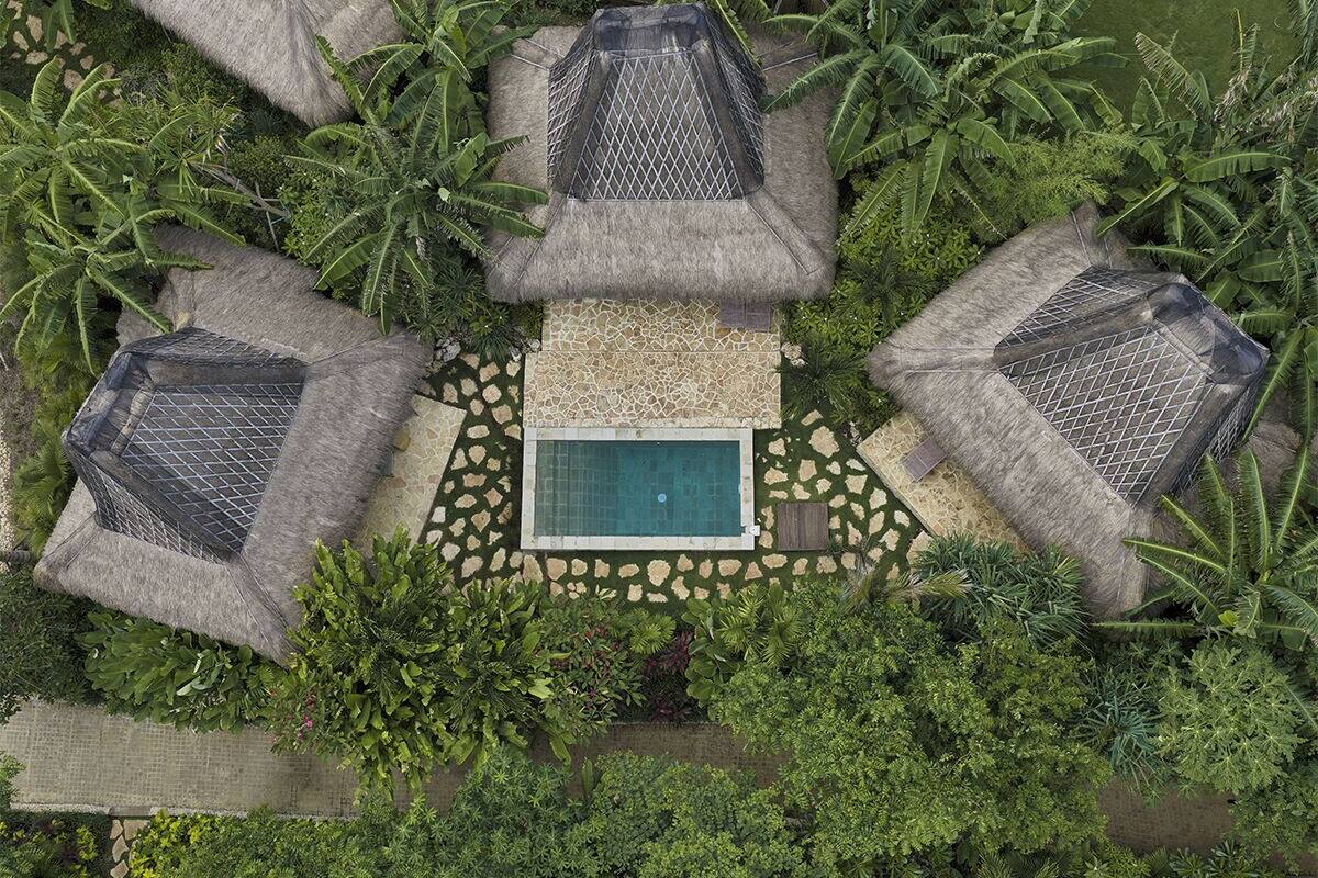 Vista aérea de un resort con una piscina central, rodeado de sombrillas de paja y exuberante vegetación tropical.