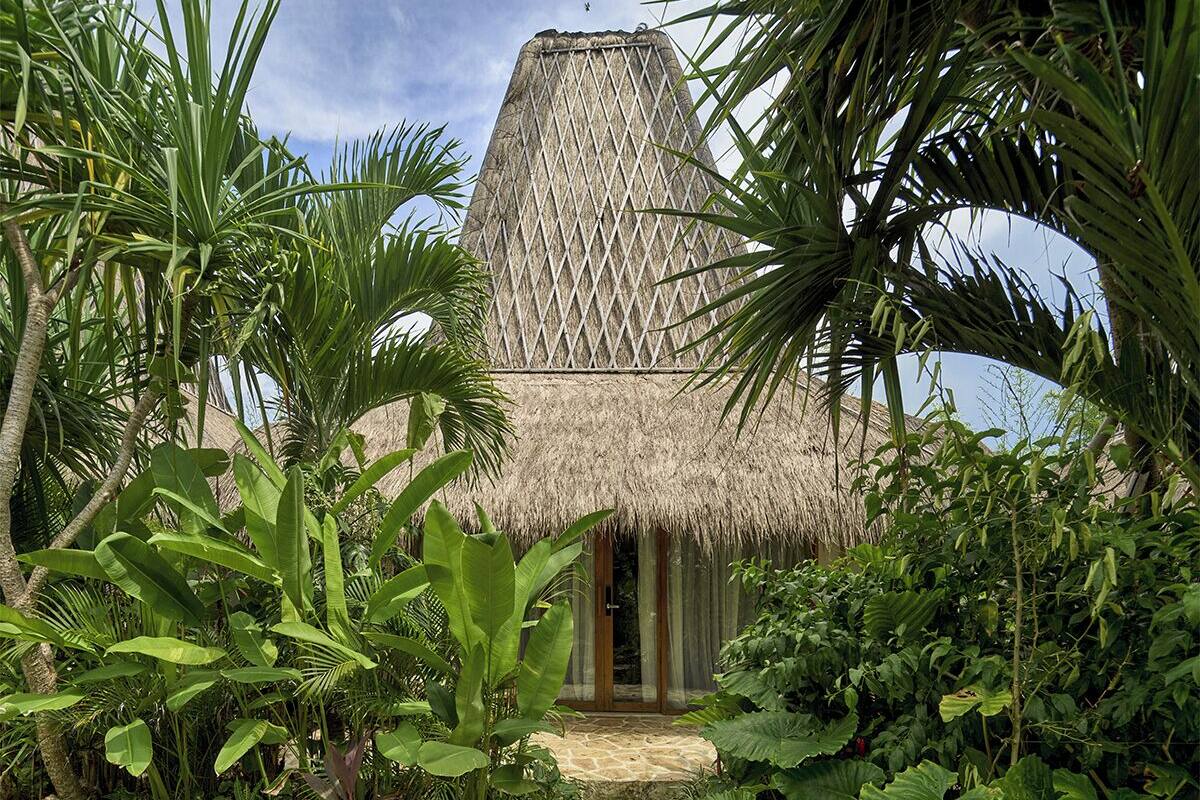 Una edificación con techo de paja rodeada de follaje tropical.
