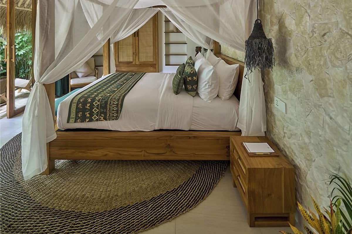 Una habitación con una cama bajo un dosel, una pared de piedra y un tapete de fibras tejidas.