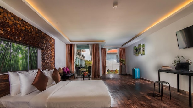 A hotel room with a large bed, a desk, a TV, and a balcony with a view. - Elysium Suite (Siem Reap)