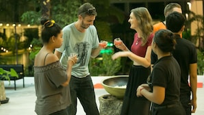 A group of people standing outdoors, some holding drinks, with a large bowl on a tree stump in the foreground. - Elysium Suite (Siem Reap)