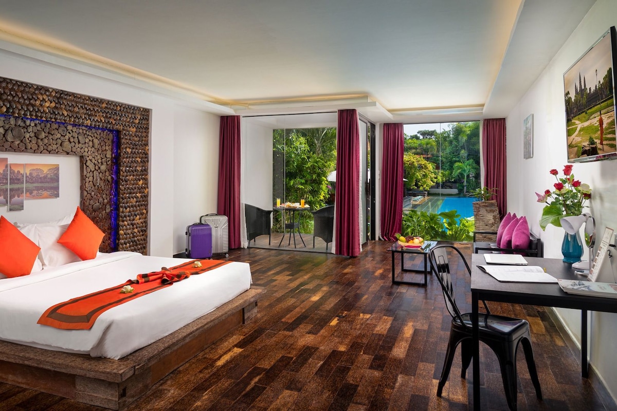 A hotel room with a bed, a desk, a chair, a suitcase, and a view of an outdoor swimming pool.